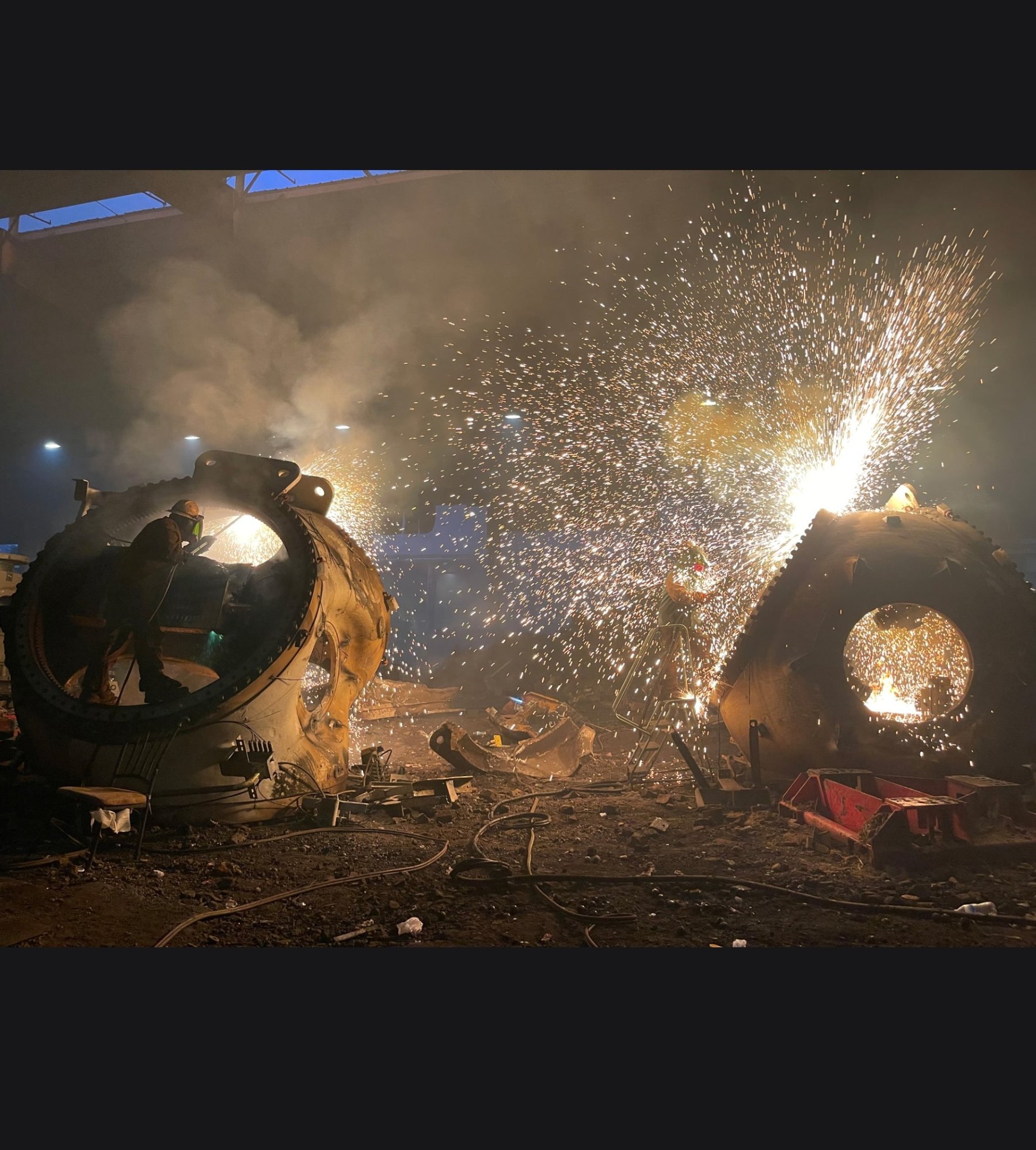 Two torch operators cutting oversized components at night with heavy sparks