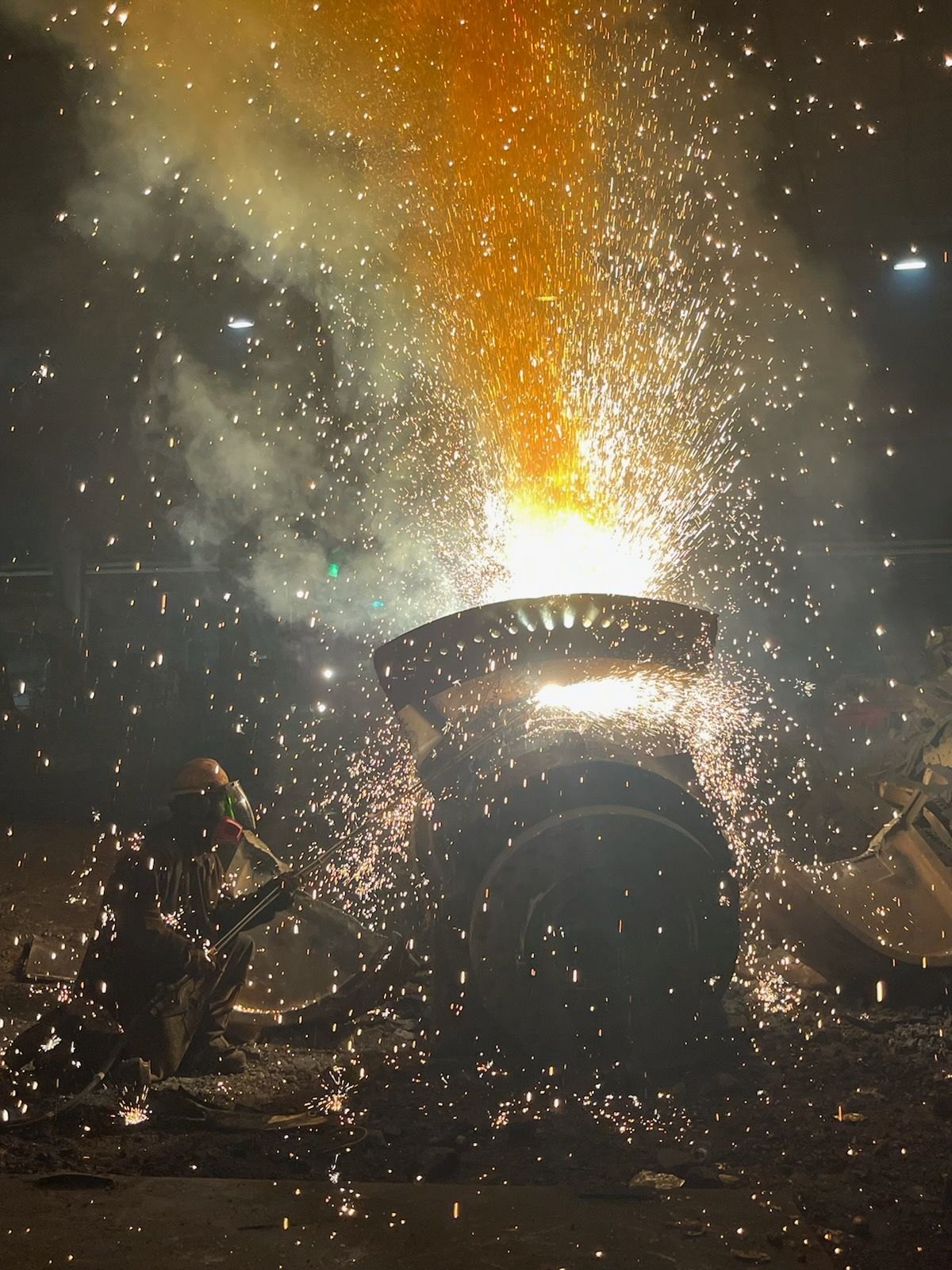Torch operator cutting a large industrial hub at night